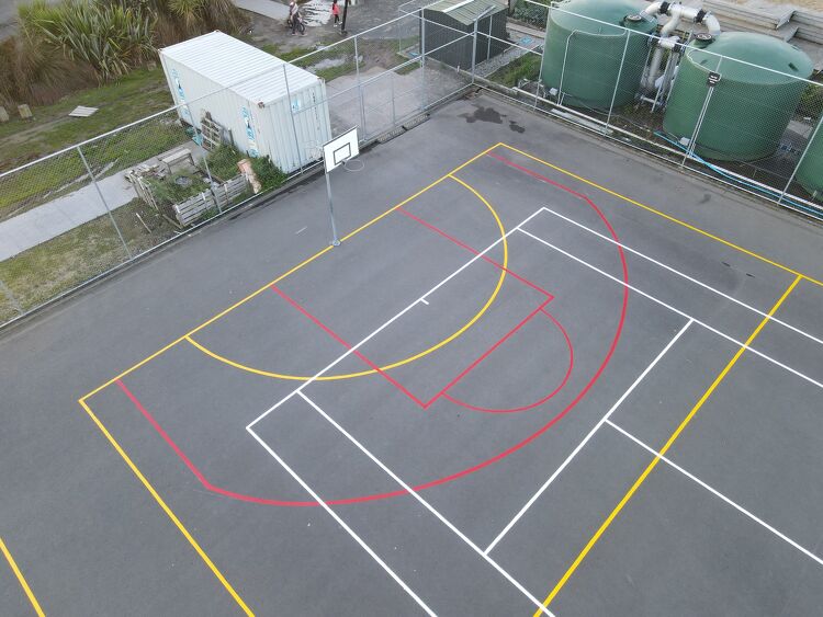 Multi-sport court with basketball and netball lines in red, yellow, and white for school use.