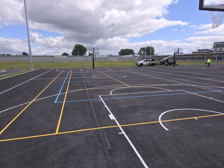 Large outdoor sports complex with new blue, yellow, and white court line markings for multiple games.