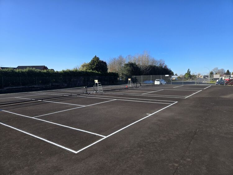 New tennis court line markings on a black asphalt surface under clear blue skies.