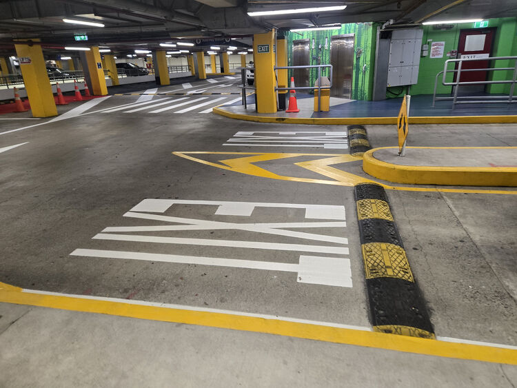 Underground car park with bright white exit markings, yellow curbs, and directional arrows for safe vehicle movement.