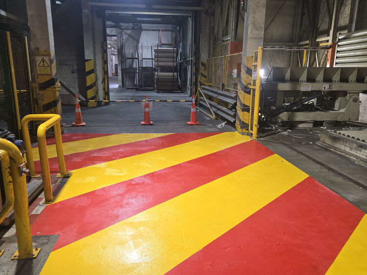 Factory floor safety markings in red and yellow stripes for hazard zone identification.