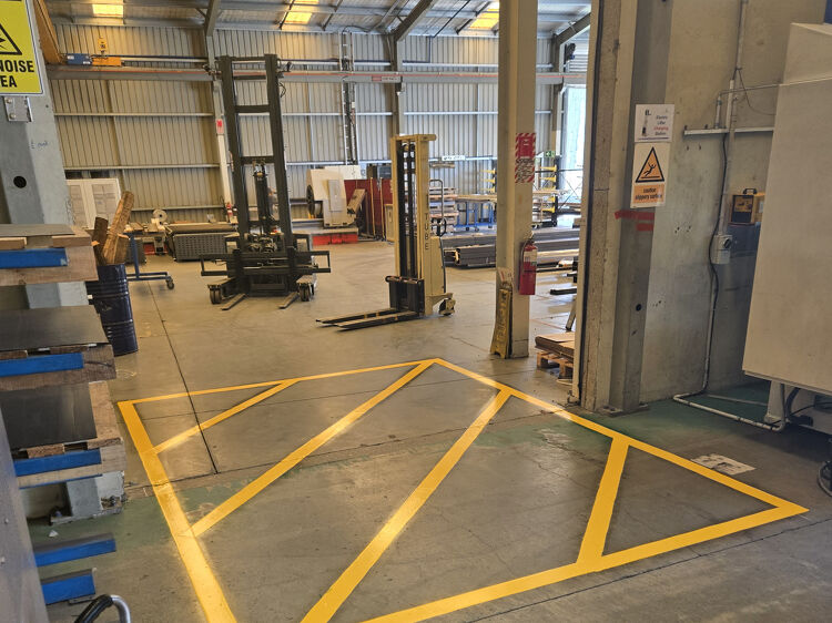 Factory floor safety zone outlined in yellow paint to restrict machinery access.